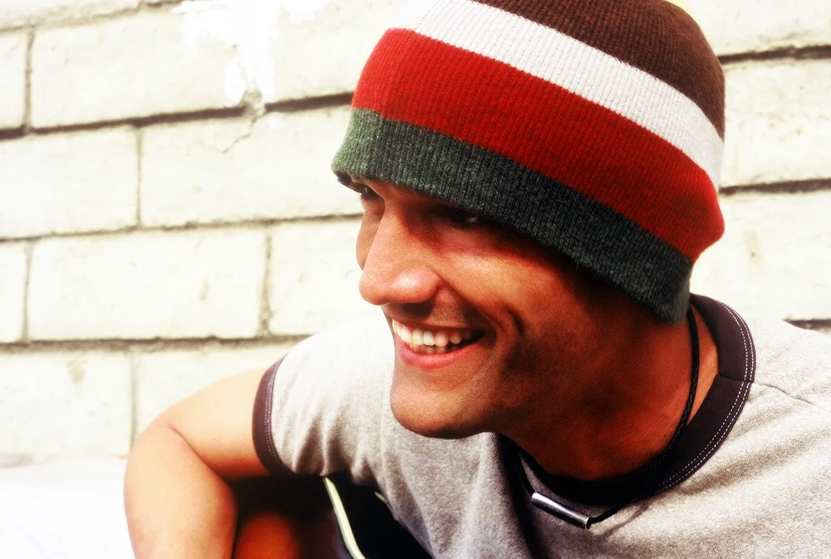 Kef laughing with an acoustic guitar against a white brick wall