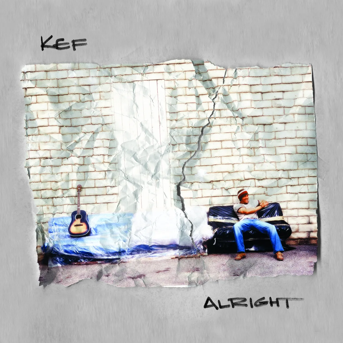 Alright album cover: Kef in a striped beanie on a plastic-wrapped couch against a white brick wall, with an acoustic guitar on a second couch
